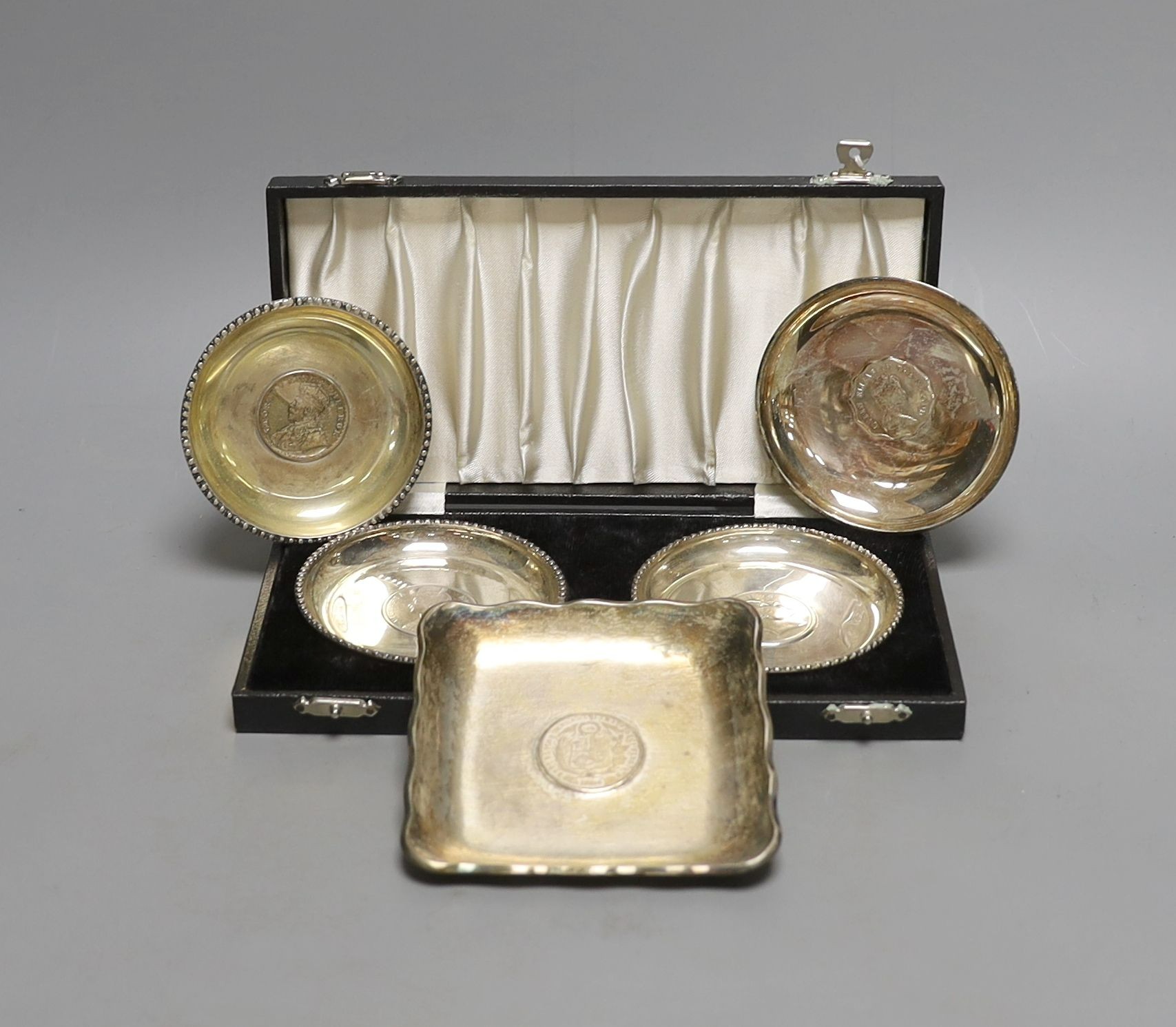 A cased pair of white metal inset coin small dishes and three other similar dishes.